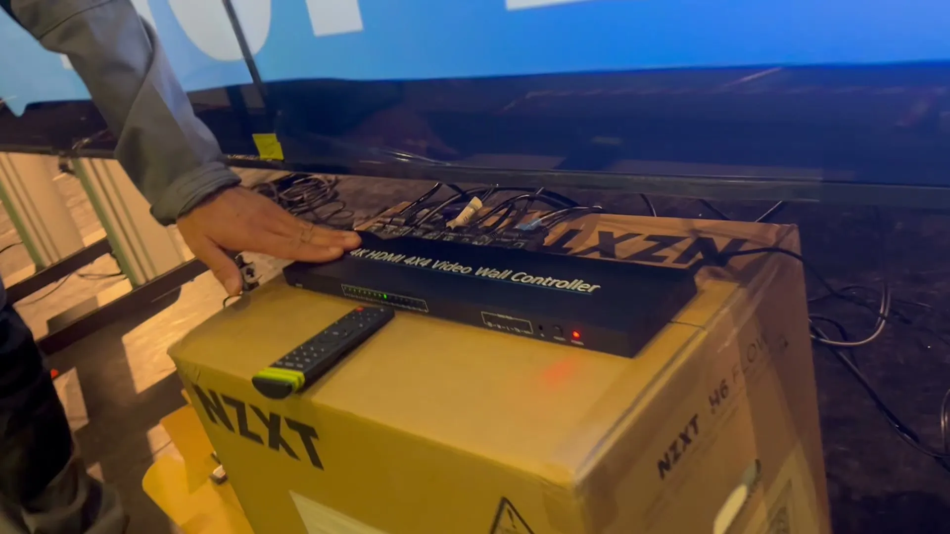 Le contrôleur de mur vidéo et sa télécommande posés sur un carton, une main dessus