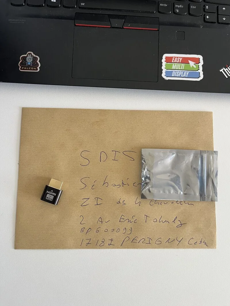 Um envelope kraft endereçado ao SDIS 17, um HDMI dummy plug 4K pousado em cima, diante de um computador portátil com o logótipo Easy Multi Display
